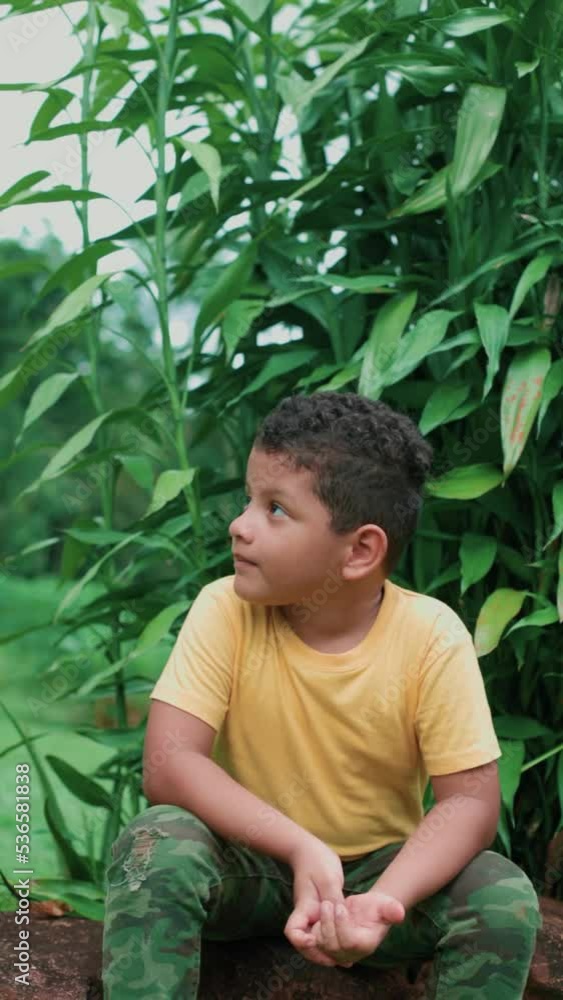 latin boy sitting on a stone talking, vertical plane