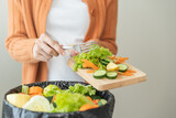 Compost from leftover food, asian young housekeeper woman hand holding cutting board use fork scraping waste, rotten vegetable throwing away into garbage, trash or bin. Environmentally responsible.