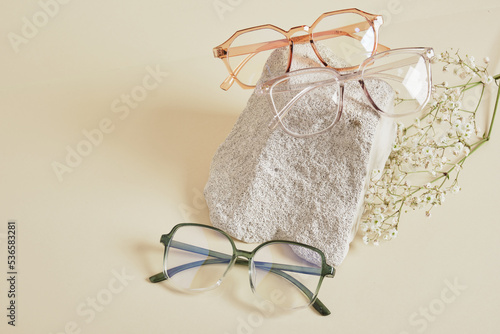 several different trebdy eye glasses with fashion frames and concrete podium on beige background