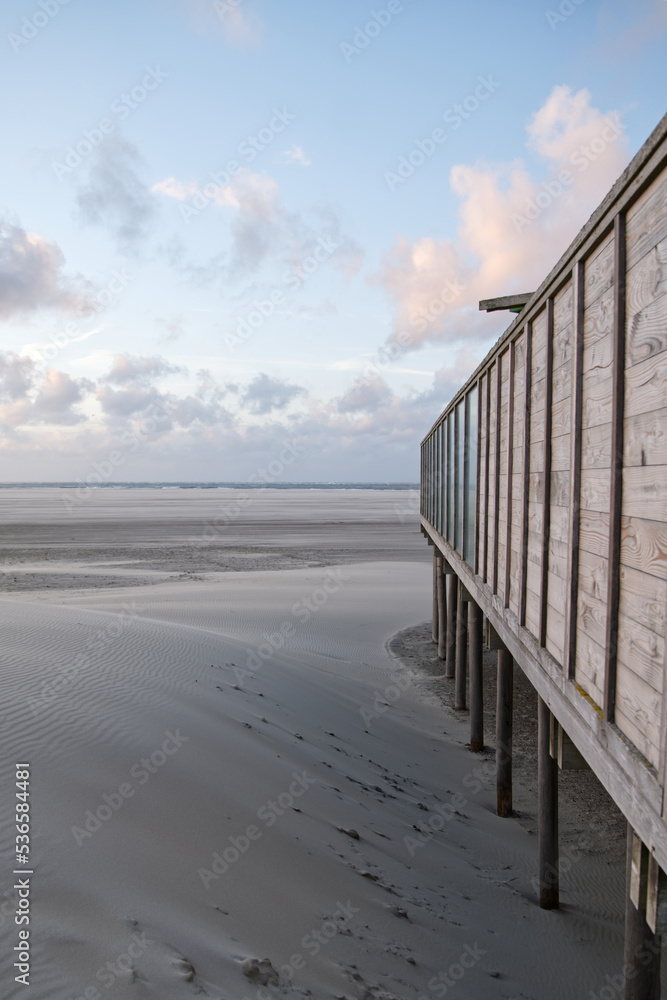 Wooden construction standing on the beach in Texel Island, Netherlands. Wooden beach pavilion on a sand dune. Sunset scene of elevated pier construction on an endless beach. Summer vacation beach. 