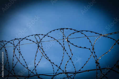 Fragment of fence made of barbed wire. Against background of blue sky. Barbed Wire Fence. Captivity, prison