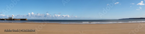 long panoramic view of the beach at Scarborough south bay on a sunlite summer day with the harbour and lighthouse in the distance photo