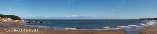 long panoramic view of the beach at Scarborough south bay on a sunlit summer day with the town harbour and lighthouse in the distance