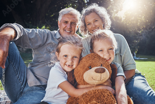 Family, children and teddy bear with a girl, grandparents and sister on the grass in a nature park during summer. Kids, haooy and love with senior man, woman and grandchildren outdoor in the day photo