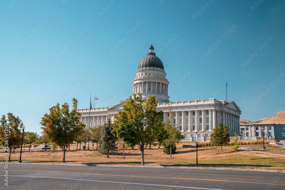 Empty road by trees at entrance of State Capitol building in Salt Lake city. View of government built structure with clear blue sky in background. Famous political landmark in city during summer.