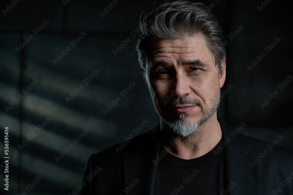 Business portrait - businessman in black jacket standing against dark gray wall. Confident middle aged, mid adult man in his 50s, smiling. Copy space. Business portrait - businessman in black jacket standing against dark gray wall. Confident middle aged, mid adult man in his 50s, smiling. Copy space.