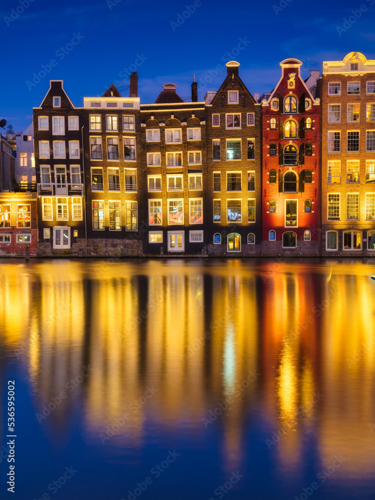 Damrak, Amsterdam, Netherlands. View of houses during sunset. The famous Dutch canals. A cityscape in the evening. Travel photography.