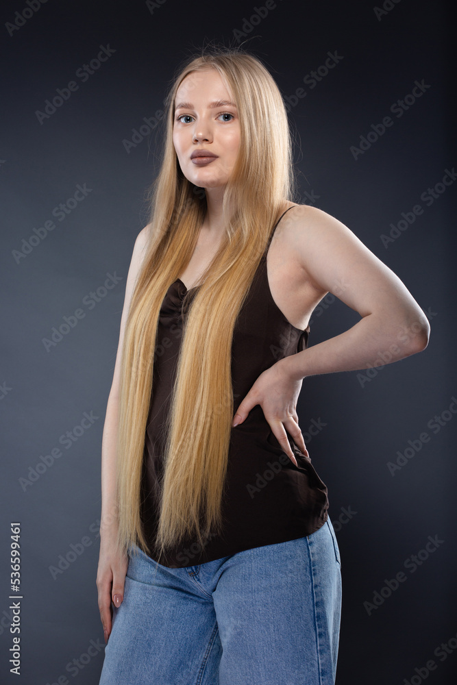 Naklejka premium Young blonde woman in jeans and brown singlet on gray background