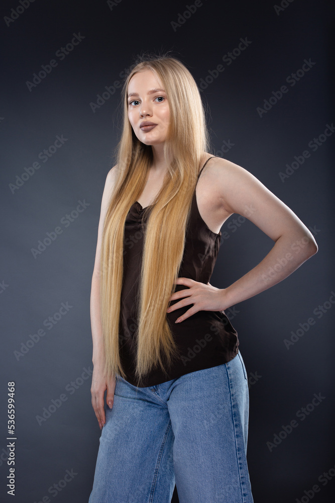 Young blonde woman in jeans and brown singlet on gray background Young blonde woman in jeans and brown singlet on gray background