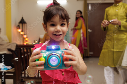 Cute little Kid, dressed up in ethnic wear playing with toy expressing emotion looking at the candle celebrating diwali Hindu festival Laxmi poojan