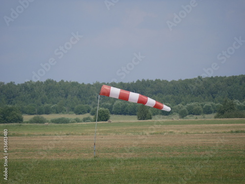 Wind direction and strength indicator on the airfield on a sunny summer day. Synthetic product made of red and white fabric.