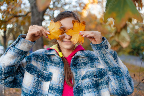 Portrait of a happy teen girl with a smile with an autumn yellow leaf in the park.