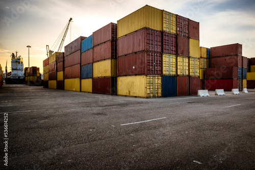 Stack of containers piled up at the port with crane loading a vessel