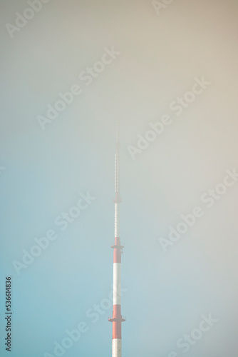 An antenna of a TV tower surrounded by clouds on a sunny morning with some blue sky
