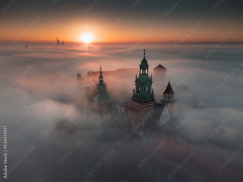 Wawel Castle in Kraków, Poland. Aerial, drone photo of the Royal Castle above the morning fog during the sunrise. - obrazy, fototapety, plakaty 