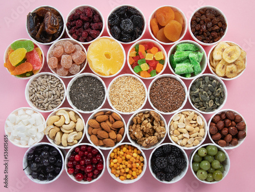 Berries  nuts  seeds  dried fruits in round containers. Background with a mix of healthy snacks. Assorted vitamin food on a pink background.