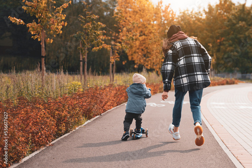 Mother help her son ride with kick scooter. Happy family mother teaches child son to ride a scooter in the Park. Support childhood parenthood idea. happy family concept