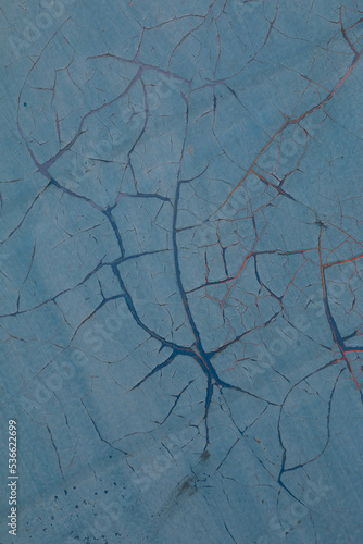 Cracked paint. A lot of cracks in paint. Missing patch of paint in the middle. Crack with flappy peeling edges. Texture of old painted wall. The background is light blue, the cracks are blue and red.