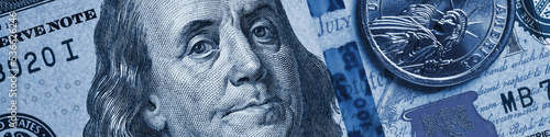 American money close-up. 100 dollar note and 1 dollar coin. Benjamin Franklin and Statue of Liberty. Blue tinted banner or header about US economy. Public debt and USA dollars. Reserve currency. Macro