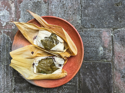 Two Oaxacan tamales with hoja santa wrapped on the outside of the masa and filled with beans with brick background photo