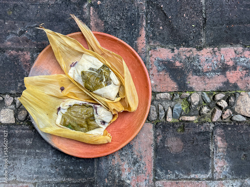 Two Oaxacan tamales with hoja santa wrapped on the outside of the masa and filled with beans with brick background photo