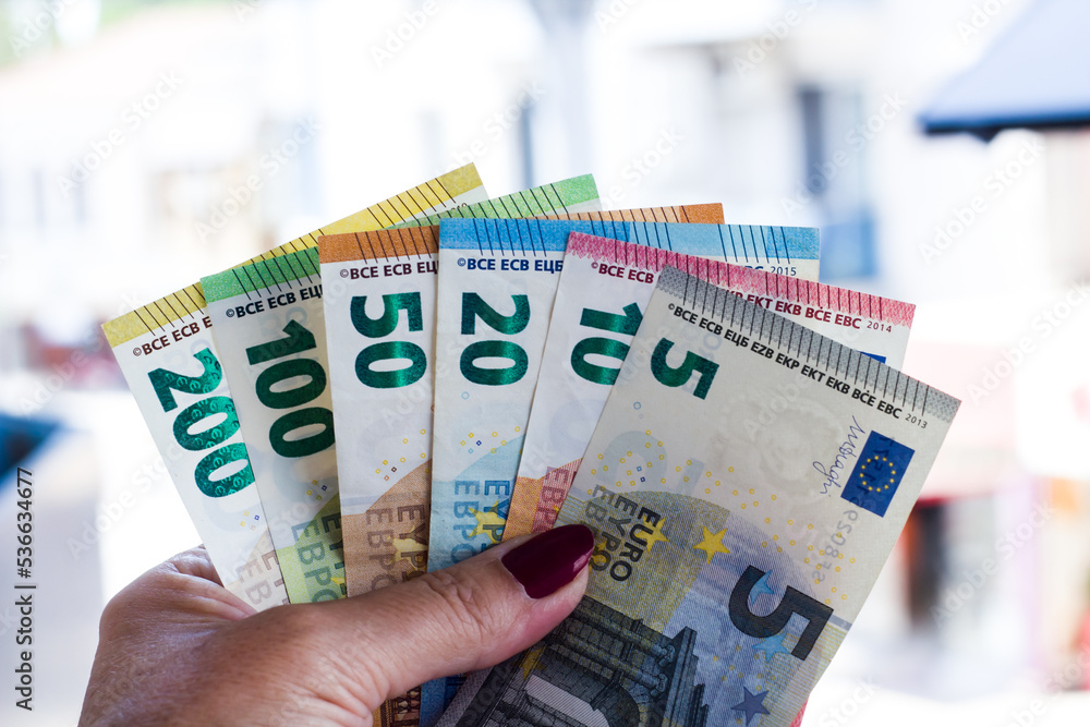 A hand with red nail polish holding  Euro Banknotes on a blur background