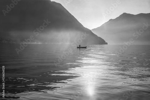 Idyllic landscape on lake Como (a little fog) with boat of fishier and small body of fisher at distance (unrecognizable person)