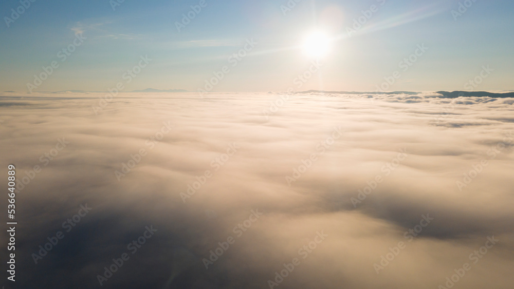 Sky, Sunrays, Sunrise and Horizon over a clouds cover mountains ridge and pipe plant, aerial