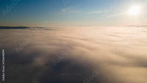 Sun, Sunrays, Sunrise and Horizon over a clouds cover mountains ridge and pipe plant, aerial view