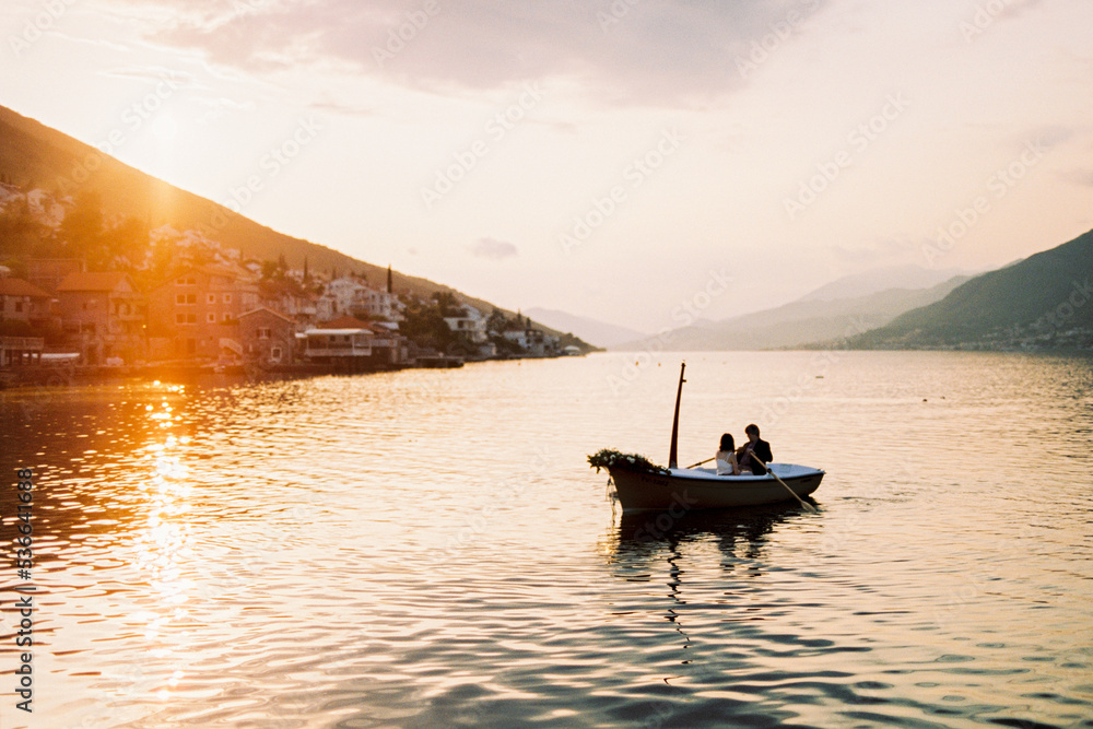 Man and woman are sailing in a boat with oars on the sea against the sunset sky