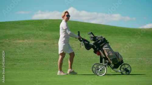 A woman walks on a golf course and pulls a cart with golf equipment