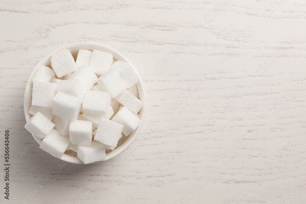 Bowl with sugar cubes on white wooden table, top view. Space for text Bowl with sugar cubes on white wooden table, top view. Space for text