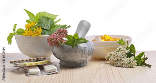 Mortar with fresh herbs and pills on white background