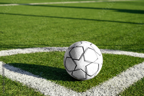 A white and black soccer ball in the corner of the field on the artificial green grass of the stadium with markings © Maryna