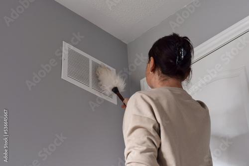 Woman cleaning return air vent with duster photo