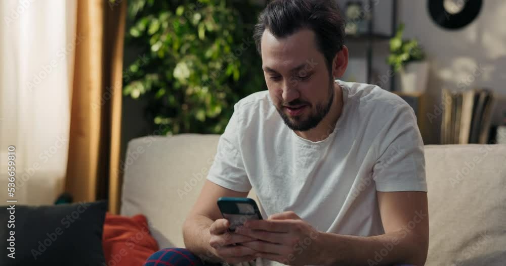 A phone user reading a text message on a screen, relaxing on the couch at home. A man focused on a smartphone, using an online application, chatting online with friends.