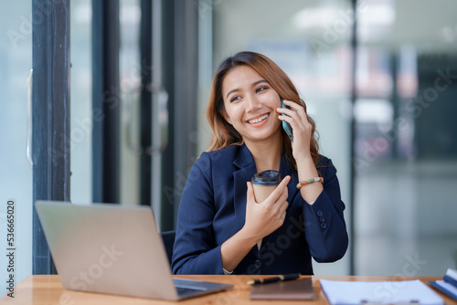 Smiling Asian businesswoman enjoying the phone, answering questions, talking to customers on the phone and comment in the office.