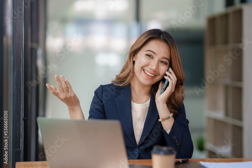 Smiling Asian businesswoman enjoying the phone, answering questions, talking to customers on the phone and comment in the office.