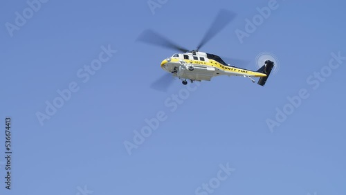 Close up bottom up view of white helicopter in slow motion flying above in clear blue sky.Los Angeles, California USA RED shot. Firefighter helicopter circling above smoking wildfire on hot summer day photo