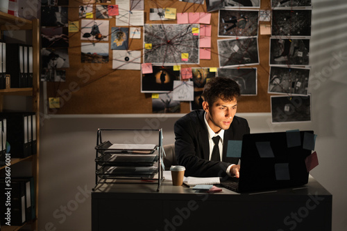 Detective working in his office using laptop, searching in internet some information