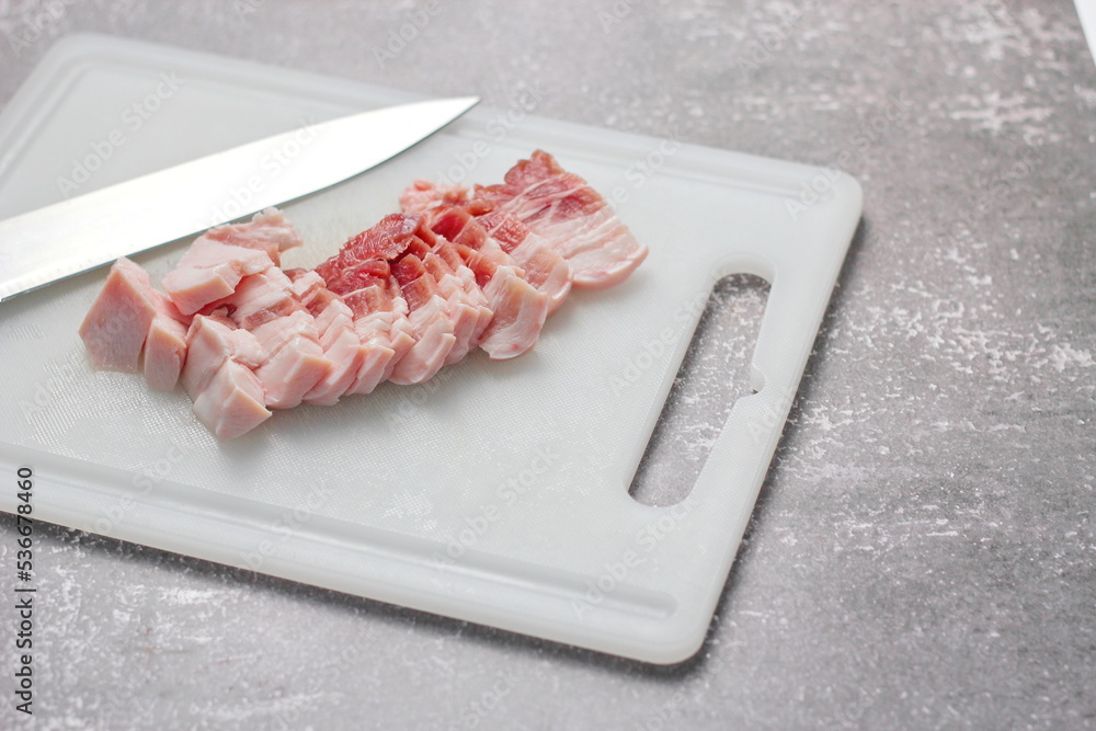 streaky pork is sliced on a white chopping board in the kitchen.Close up cutting slide pork belly raw streaky pork is sliced on a white chopping board in the kitchen.Close up cutting slide pork belly raw