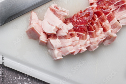 streaky pork is sliced on a white chopping board in the kitchen.Close up cutting slide pork belly raw