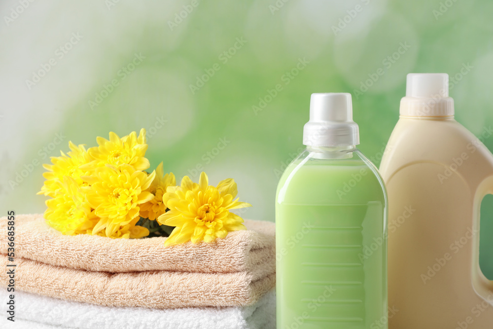 Bottles of laundry detergents, towels and beautiful flowers on blurred background, closeup Bottles of laundry detergents, towels and beautiful flowers on blurred background, closeup