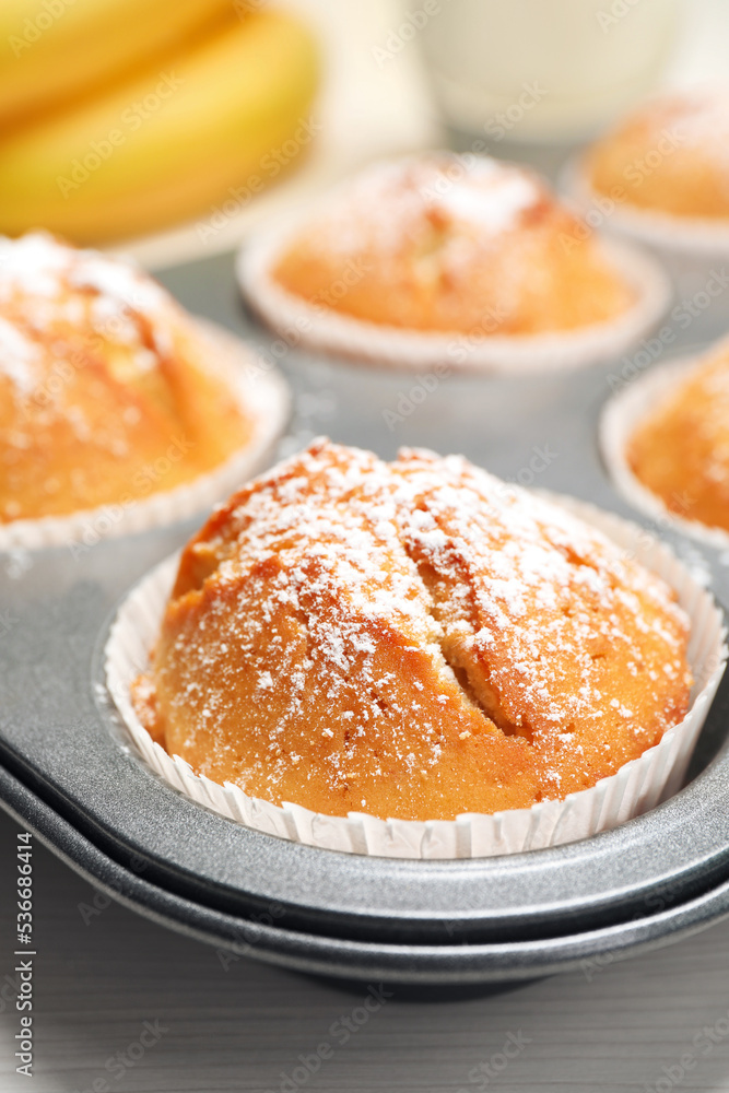 Tasty homemade banana muffins powdered with sugar in tray on white wooden table, closeup