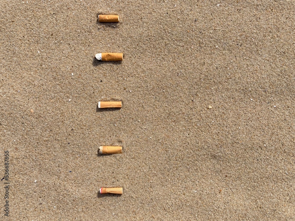 five cigarette butts arranged as bullet points in sand on beach five cigarette butts arranged as bullet points in sand on beach