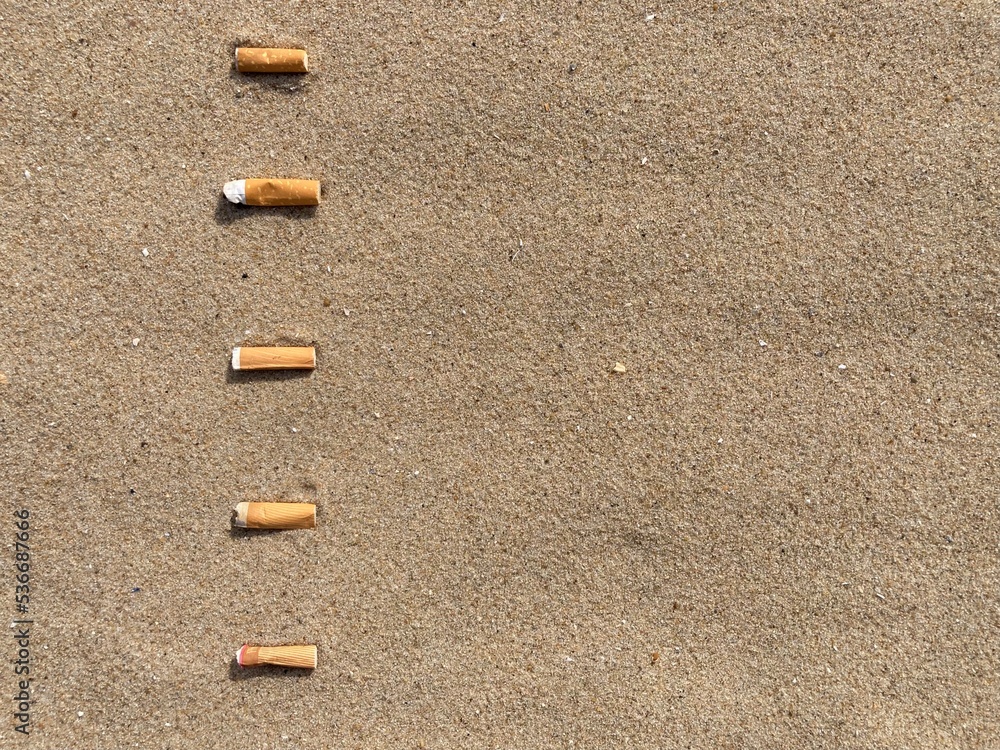 five cigarette butts arranged as bullet points in sand on beach five cigarette butts arranged as bullet points in sand on beach