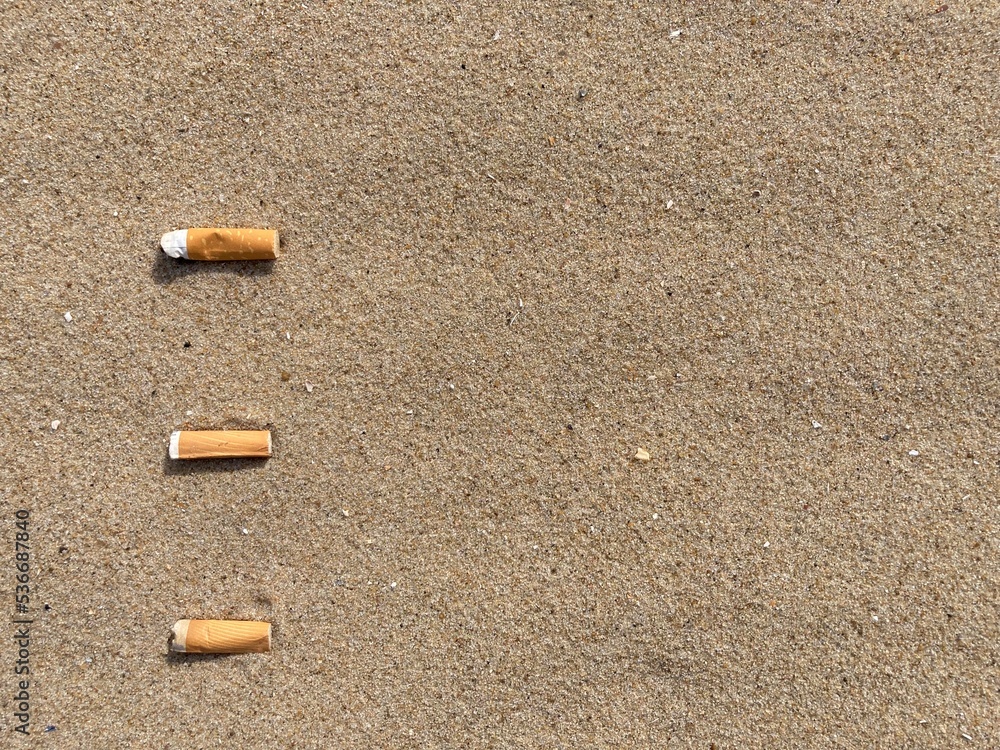 three cigarette butts arranged as bullet points in sand on beach three cigarette butts arranged as bullet points in sand on beach