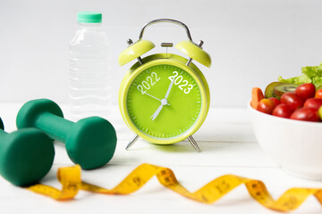 2022 and 2023 on alarm clock with workout planing for dieting. Sport exercise equipment workout and gym nutrition fresh salad for fitness. Merry Christmas and Happy new year concept