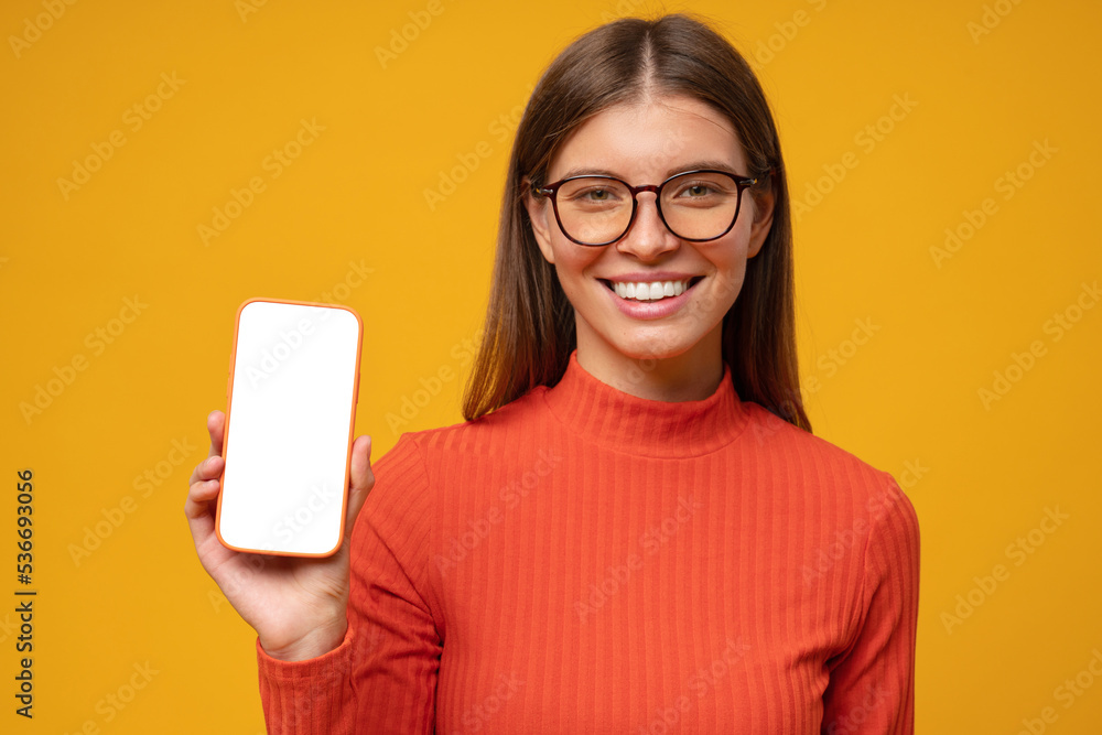 Portrait of smiling happy young woman holding blank phone screen, isolated on yellow background Portrait of smiling happy young woman holding blank phone screen, isolated on yellow background