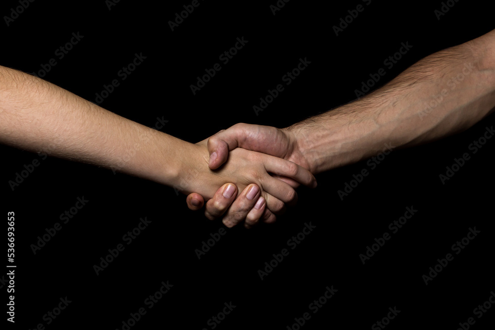 A man's hand squeezes a woman's hand on a black background. The concept of agreement and equality
